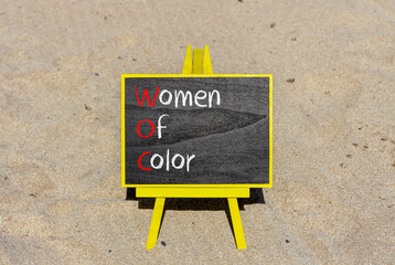 WOC women of color symbol. Concept words WOC women of color on beautiful yellow blackboard. Beautiful sand background. Business WOC women of color social issues concept. Copy space. - obrazy, fototapety, plakaty