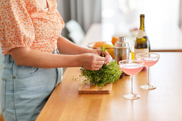 drinks and people concept - close up of woman with thyme and glasses making cocktails at home kitchen