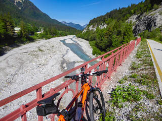 Mountain bike mtb leaning against iron bars of bridge along the Alpe Adria trail in Friuli-Venezia Giulia, Italy, Europe. Braided river Tagliamento running through wild mountainous landscape. Awe