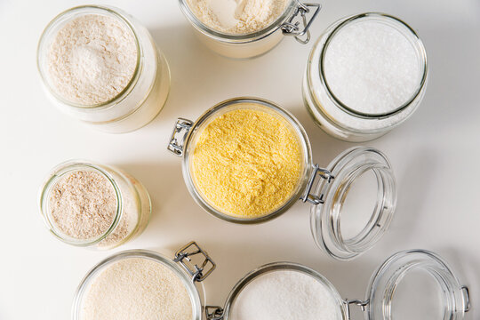 food storage, culinary and eating concept - close up of jars with different kind of flour, salt and sugar on white background, top view