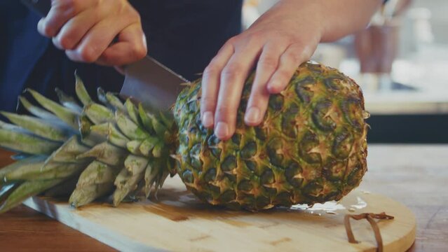 Close up of woman's hands cutting pineapple in half using a knife. Female cook, chef in a brightly lit kitchen. Studio shot. High quality 4k footage