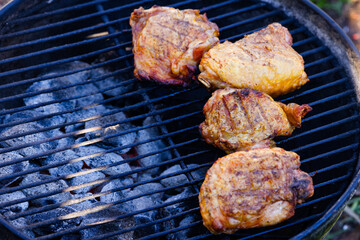 Chicken thighs cooking on a charcoal grill with hot coals in view. Selective focus, background blur, foreground blur