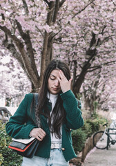 Portrait of a brunette in a green jacket against the background of cherry blossoms.