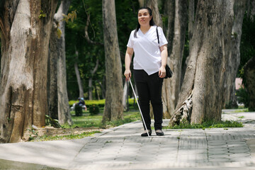 Woman with blindness disability walking on sidewalk contain tactile paving guide blocks using long white cane or blind cane a mobility tool to detect objects in the path for vision impairment people