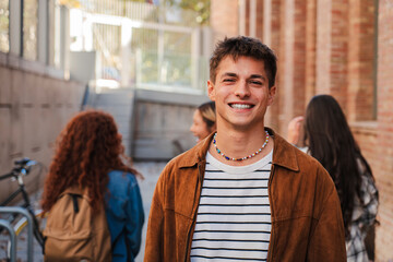 Portrait of one student teenage male smiling and looking at camera at university campus. Guy standing and staring front with positive expression at high school. Confident happy young man at academy