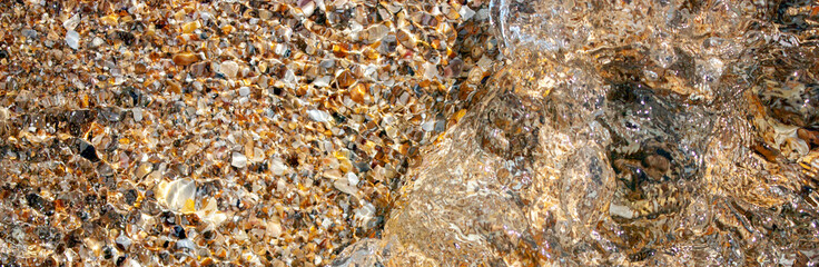 Reflection in the water of a stone texture in the light of the sun. Waves at sea and natural stones. Different colors and a unique pattern of sea waves on a sunny day.