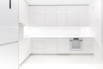 Front view of a modern luxury trendy snow white kitchen with many cabinets, glossy lacquered...