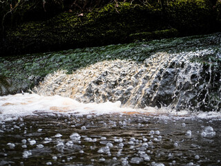 Closeup of fast running river water, White water flowing along the river bank. water splashes over...