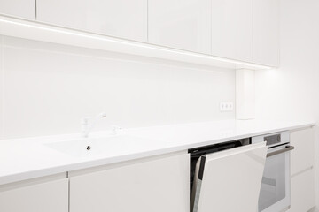 Modern white kitchen interior with acrylic countertop and built in stone sink and opened door of washing machine, luxury monochrome design, image with selective focus