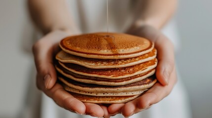   A person closely holds a towering stack of pancakes, syrup visibly dripping from the peak