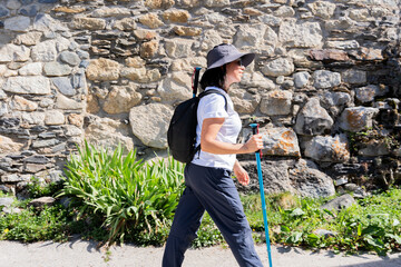 Hiker woman with hiking stick and backpack passing through a small mountain village on her trekking...