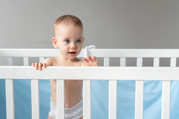Interested baby leaning on the back of a wooden crib