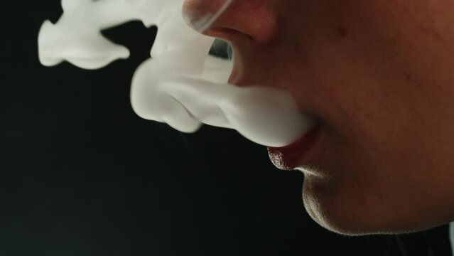 Young woman smoking hookah or cigarette on black background close-up. Smoke, vapour and fog texture.