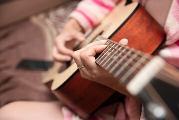 A woman is relaxing at home playing the guitar, learning a new melody. Playing the guitar is a new hobby for a woman, for self-development and relaxation, self-development concept