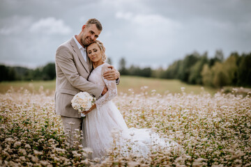Valmiera, Latvia - August 10, 2023 - Couple embracing in a wildflower field under a cloudy sky.