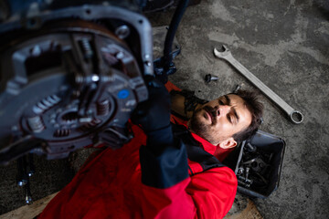 Experienced mechanic working under vehicle servicing the engine in workshop.