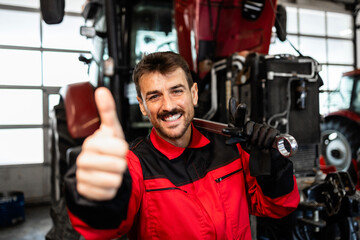 Mechanic standing in front of the tractor and showing thumbs up. Service and maintenance of agricultural machinery.