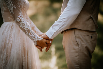Valmiera, Latvia - August 10, 2023 - Close-up of a bride and groom holding hands, focus on hands...