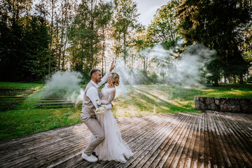 Valmiera, Latvia - August 10, 2023 - Bride and groom dancing on wooden stage, smoke around, forest...