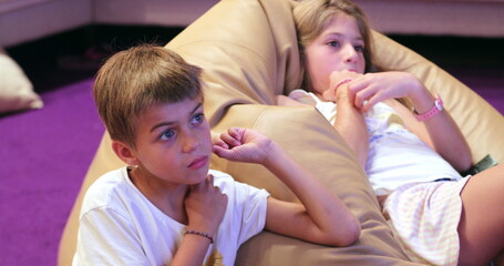 Candid children watching movie TV screen in living room kids seated on sofa