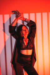 Pretty woman in black satin suit in orange light. Stylish woman in a suit against the background of studio lighting