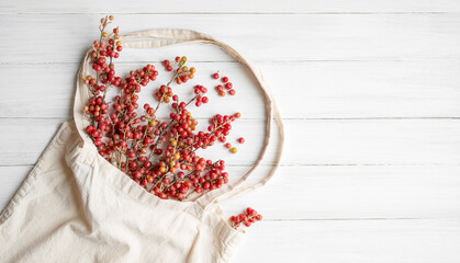 A bouquet of twigs with red sea buckthorn berries, Shepherdia argentea in a linen bag on a white painted wooden surface close-up, copy space. Alternative medicine