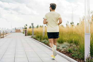 A runner is seen from behind, moving briskly along a path bordered by ornamental grasses under a...
