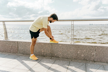 A man stretches against a railing by the sea, preparing for a run under a spacious sky.