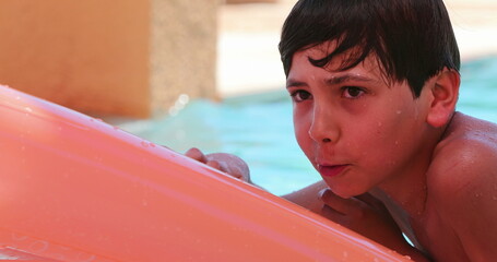 Candid child boy playing at the swimming pool on top of inflatable mattress