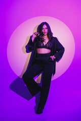 A beautiful young woman in a black suit stands on a white background. Hard light.