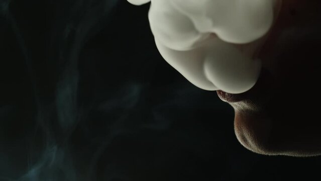 Young woman smoking hookah or cigarette on black background close-up. Smoke, vapour and fog texture.