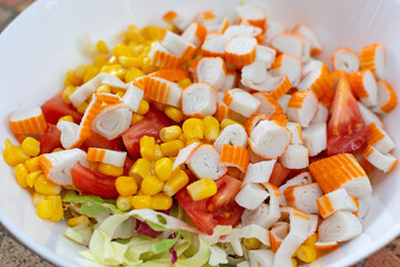 A visually appealing salad, comprised of crab sticks, corn, and fresh green lettuce, is served on a white plate