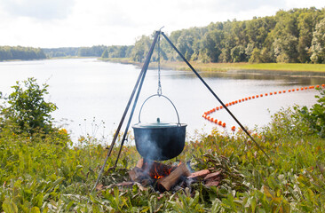 Cooking soup in a cauldron over an open fire in nature. bonfire on the shore of the lake. A cast...