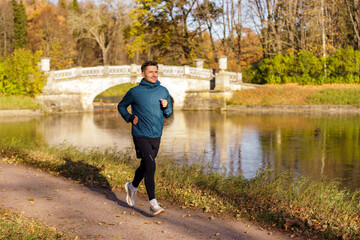 Fototapeta premium A man enjoys a run in a picturesque park, with an ornate bridge and reflective water enhancing the scene.