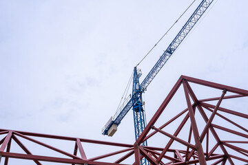 Geometric composition of red metal beams and a blue crane in a modern construction against a clear sky with copy space