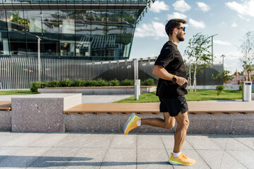 A man in motion, his black attire contrasting with vibrant sneakers, runs through a sleek urban...