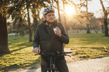 Man With Cup of Coffee Standing Next to Bicycle in a Park at Sunset