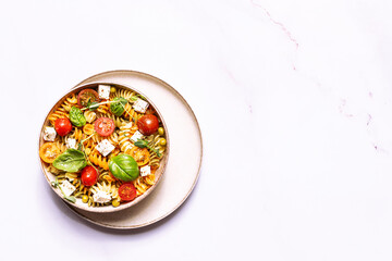 Colorful full grain fusilli pasta warm salad with feta cheese, cherry tomatoes, herbs, green pea...