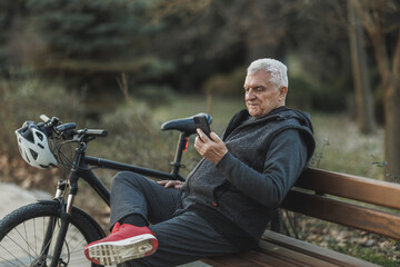 Old Man Sitting Next to Bicycle on Park Bench Using Cell Phone