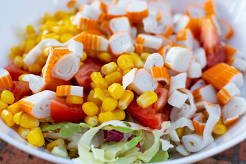 Multi-colored appetizing salad with crab sticks, corn and green lettuce in a white plate, close-up