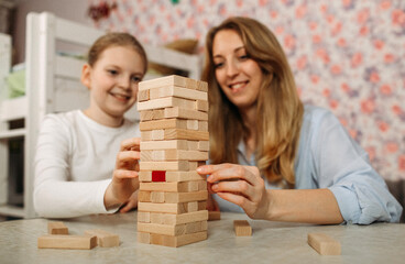 Mother and daughter playing a game with wooden blocks at home.