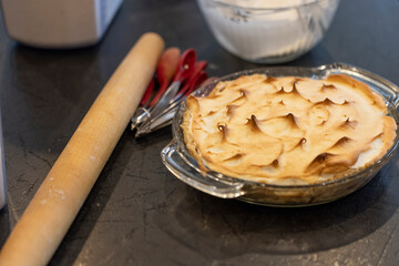 A chocolate Meringue Pie, freshly baked, ready to be served, placed on the counter with the raw ingredients that are in the pie. 