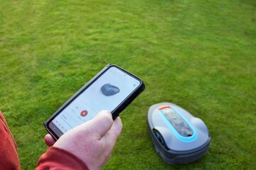 A man controls a robotic lawnmower using a phone app.