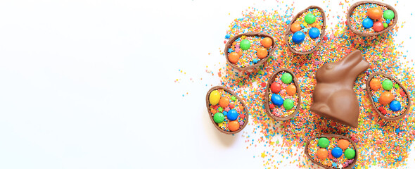 Chocolate eggs and rabbit, sugar colored sprinkles on a white background, top view. Easter...