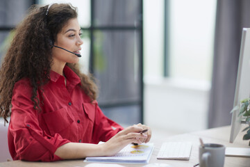 Woman wearing headphones and makes notes in notebook