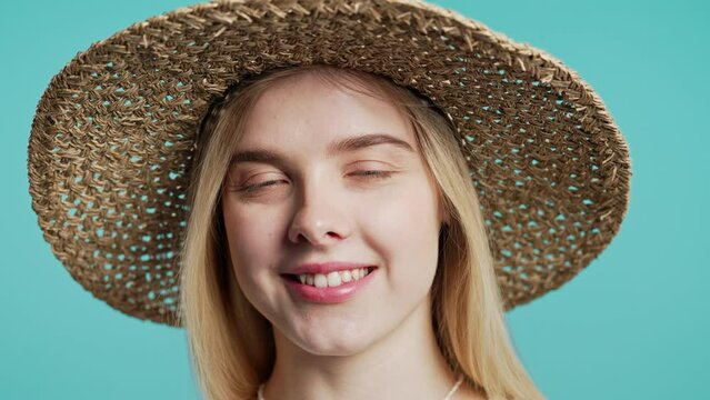 Young pretty woman smiling in straw hat looking to camera on blue background.