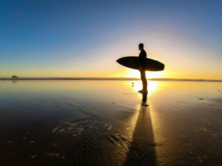 Surfer man standing in the beach at sunset. New Zealand