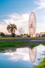 Ferris wheel in the Georgian city of Batumi. The Ferris wheel is reflected in a puddle after the...