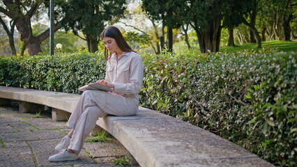 Focused reader studying book in green garden. Serene woman sitting park bench