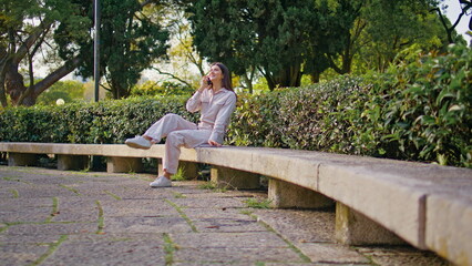 Calling woman sitting park bench enjoy mobile conversation at sunny morning.
